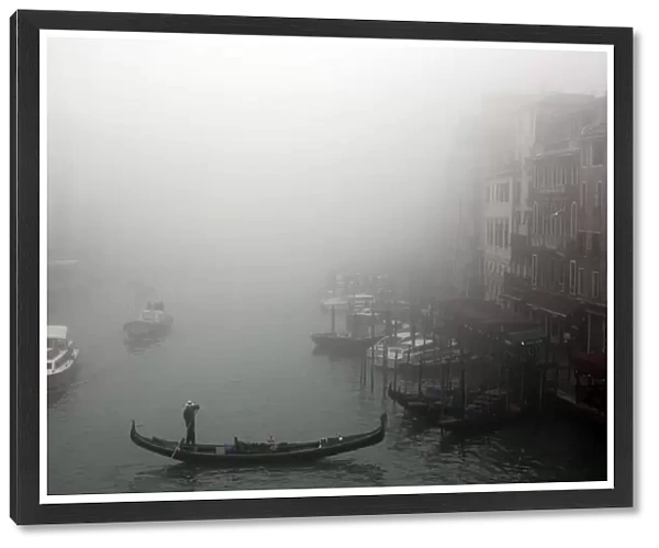 A gondolier rows his gondola across the Grand Canal in the fog in Venice