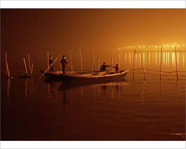 Boys tie their boats as fog covers the banks of the Yamuna river on a cold evening