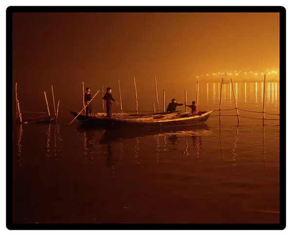 Boys tie their boats as fog covers the banks of the Yamuna river on a cold evening
