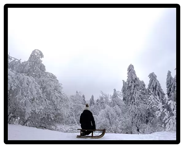 A young girl sits on her sledge on top of the Feldberg mountain during a winter day