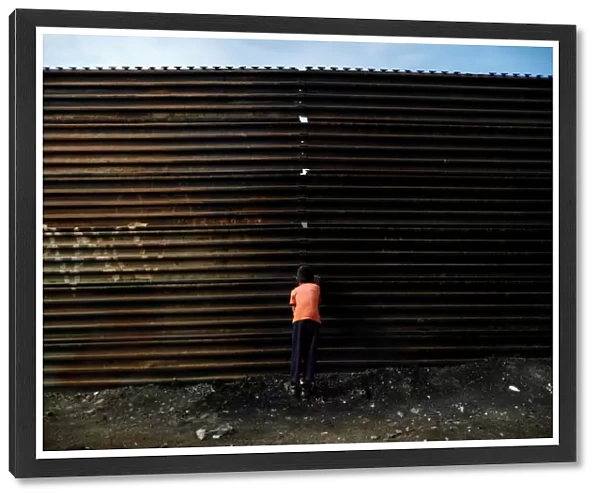 A boy looks through a hole in the current U. S. -Mexico border fence