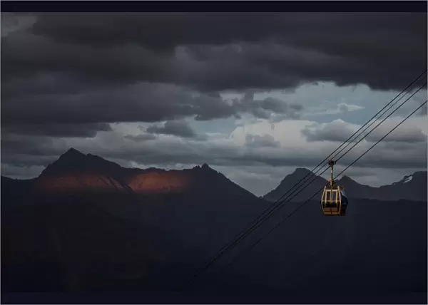 A cable car is pictured with Caucasus mountains during sunset in the background outside
