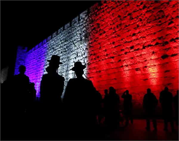 People walk past the walls of Jerusalems Old City lit in blue, white and red