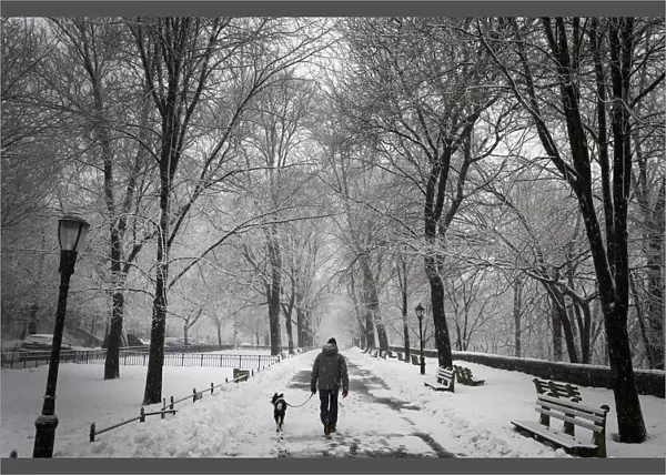 A man walks his dog in falling snow in Riverside Park in upper Manhattan in New York City