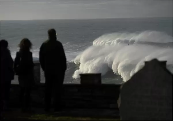 People look at waves as they crash against a lighthouse in the port town of Tapia de