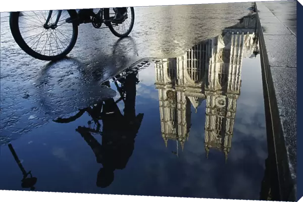 A cyclist is reflected in a puddle as he passes Westminster Abbey in London