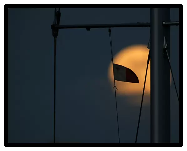 A Maltese flag flies from a yachts mast as a supermoon full moon rises in Pieta