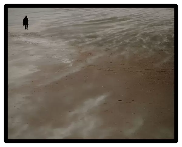 A woman walks along the beach through blowing sand in New Brighton