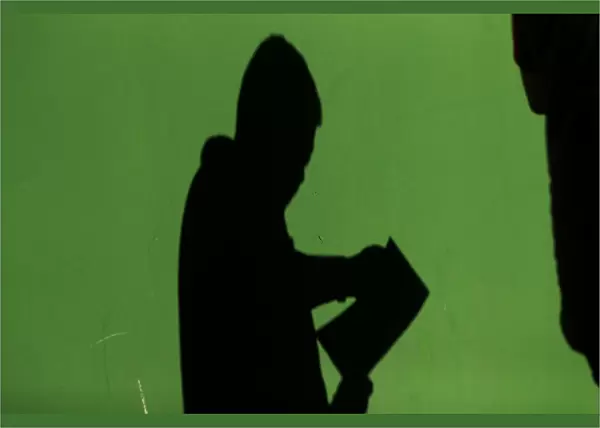 The shadow of a man is cast on a wall as he checks his documents after leaving a
