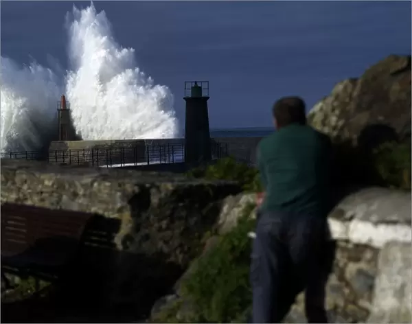 A man looks at waves as they crash against a lighthouse in the port town of Viavelez