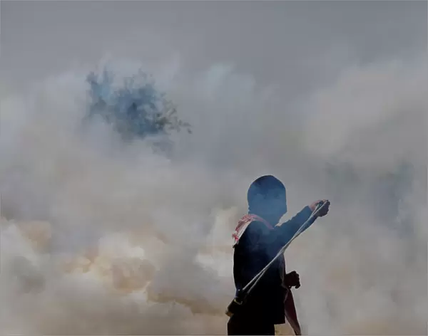 Palestinian demonstrator returns a tear gas canister fired by Israeli troops during