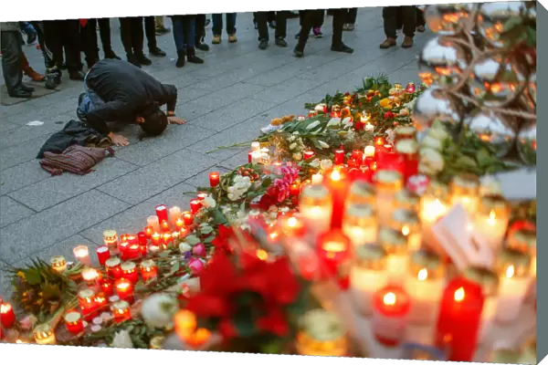 A mourner knees in front of candles, flowers and Christmas tree balls at the Christmas