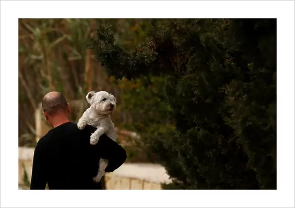A man carries his pet dog while walking in Marsaxlokk