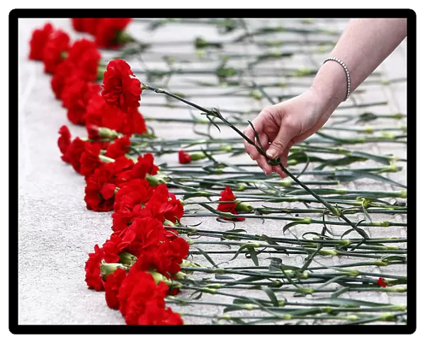 A woman places a red carnation flower on the ground by a pool outside the Scottish
