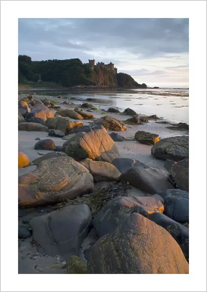 View of rocks on beach and clifftop castle at sunset, Culzean Castle, South Ayrshire, Scotland, june