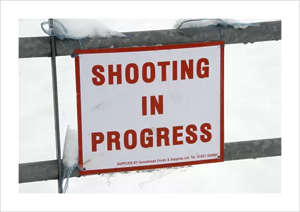 Shooting In Progress sign tied to gate in snow, warning of nearby shoot, near Mayfield, East Sussex, England, January