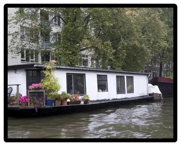 A white houseboat with lots of pink flowers surrounded by trees