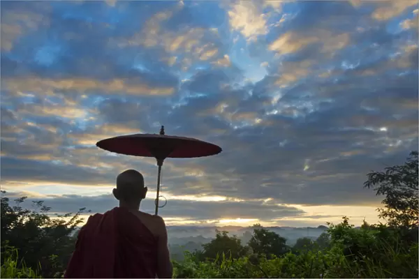 Monk with umbrella watching ancient temple and pagoda in the jungle at sunrise, Mrauk-U