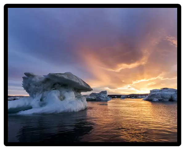 Canada, Nunavut, Territory, Setting midnight sun lights clouds above melting iceberg