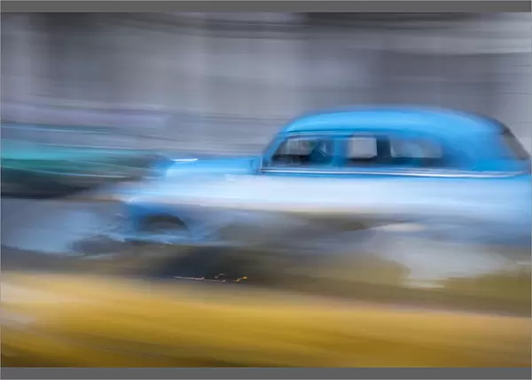 Cuba, Havana. Classic cars speed by in a blur along the streets of the city