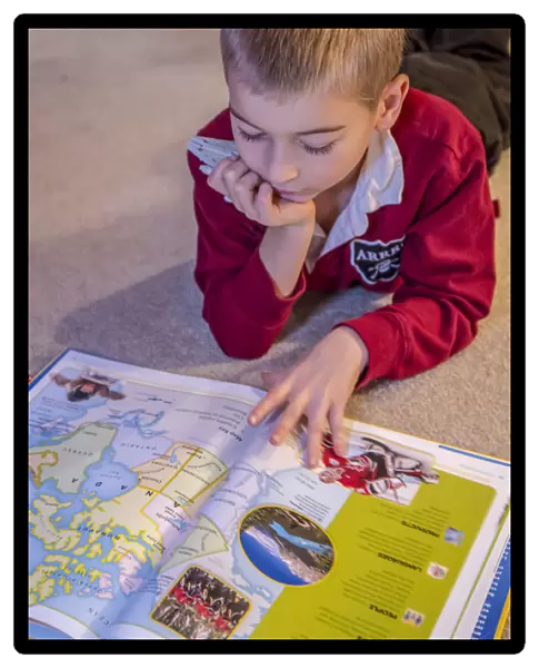 Seven year old boy reading his world atlas book. (MR)