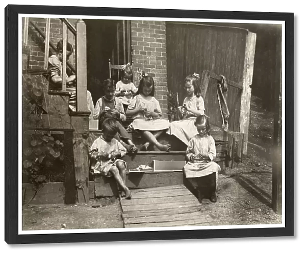 A mother with her six children working on garment tags on a tenement stoop in Roxbury, Massachusetts. Photograph by Lewis Hine, August 1912