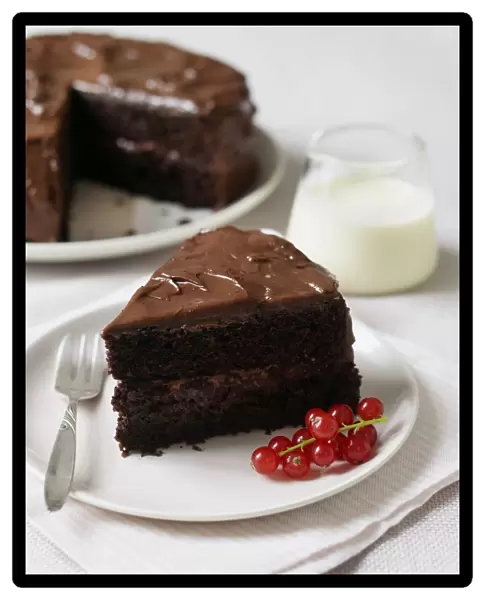 Piece of gluten-free chocolate cake on a plate with redcurrants, jug of cream and cake in background