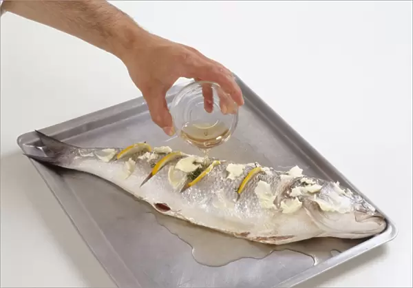 Pouring white wine over French sea bass with lemon slices in cuts on side and butter