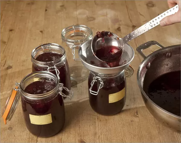 Spooning plum and cinnamon jam into sterilized jars, using ladle and funnel