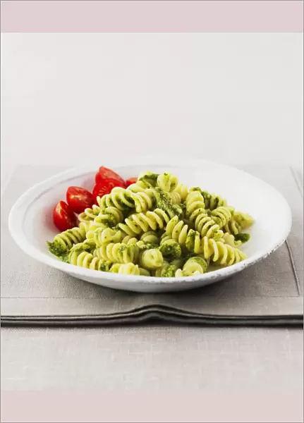 Bowl of fusilli pasta with pesto sauce and cherry tomatoes