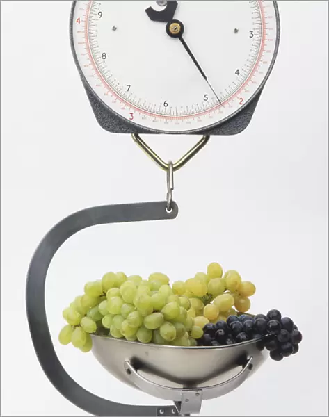 Hanging scales with metal bowl containing green and purple grapes, front view