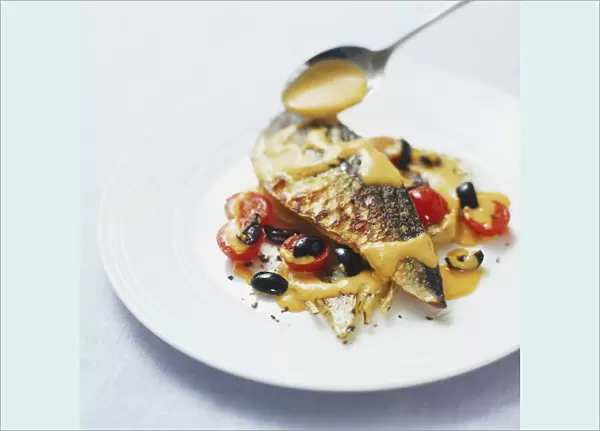 Romesco sauce being spooned over grilled mackerel fillet served with black olives and cherry tomatoes