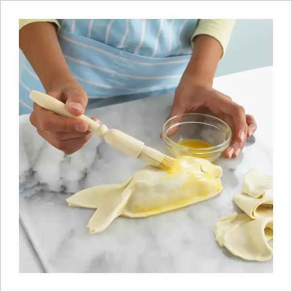 Girls hand coating fish-shaped puff pastry with butter, using a basting brush, close-up