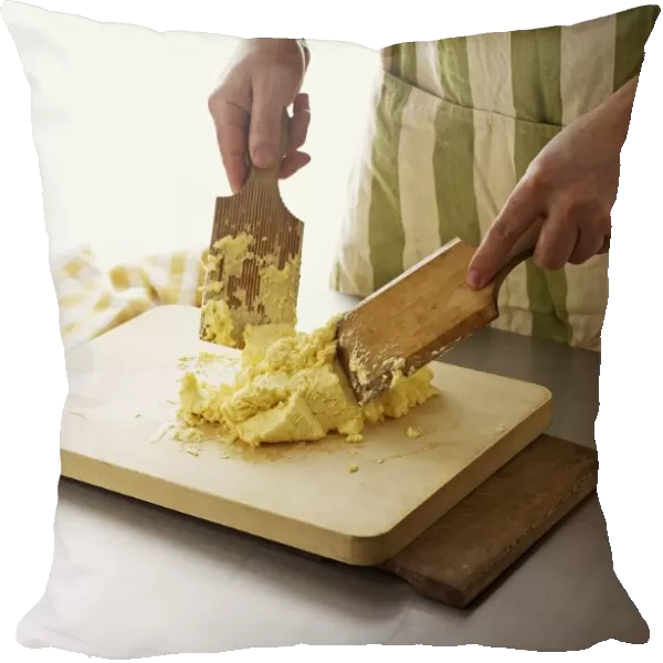 Using pair of wooden paddles to shape butter on chopping boards