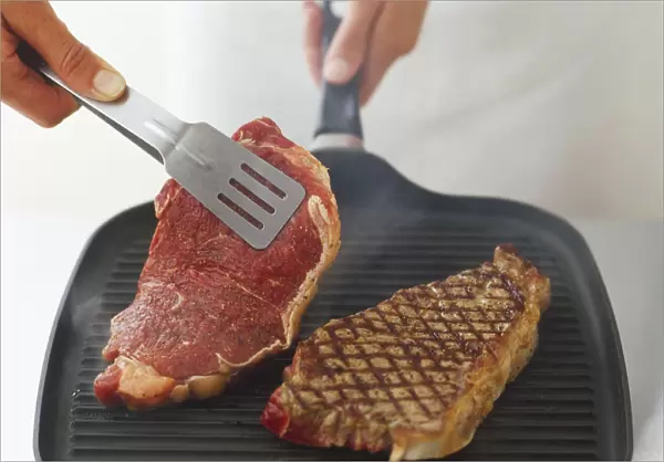 Using tongs to turn over steaks being char-grilled on a ridged, cast-iron grill pan