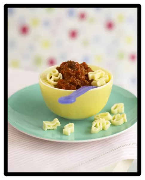Animal shape pasta with Bolognese sauce in bowl, with plastic spoon, on top of a plate