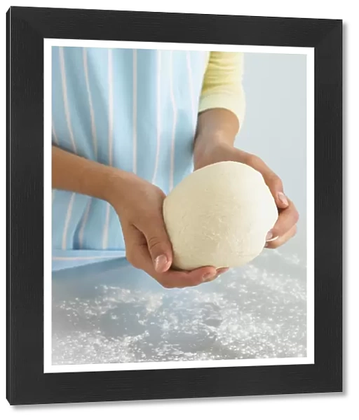 Girls hands holding ball of bread dough above floured worktop, close-up
