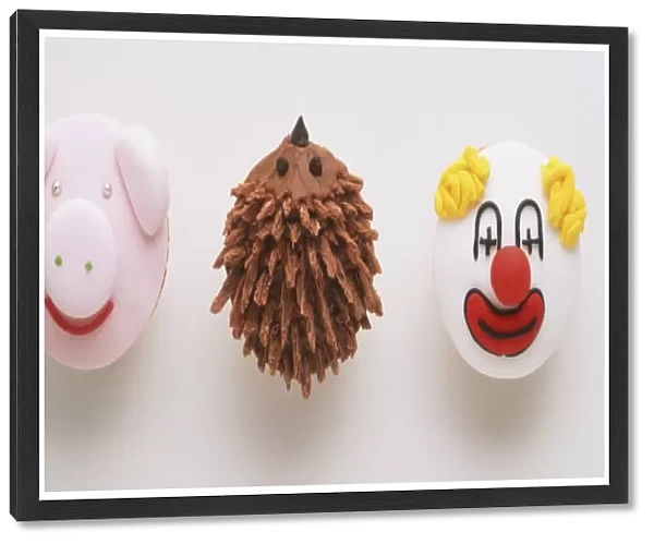Three cupcakes decorated with the face of a pig, a clown and a hedgehog, view from above