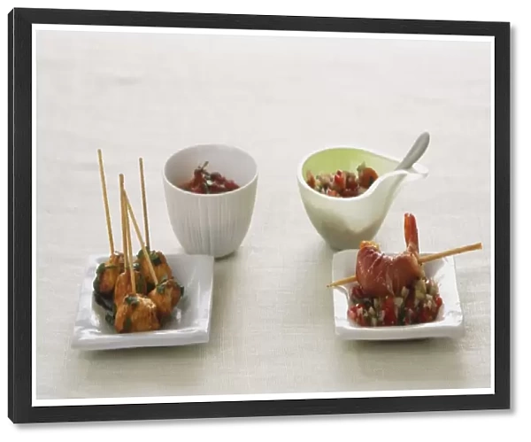 Chicken pieces on skewers on small square plate and bowl of sauce, king prawn on skewer on bed salsa on small square plate, bowl containing salsa and spoon