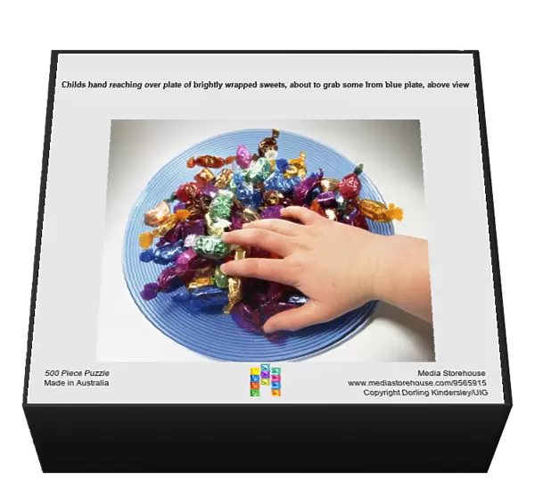 Childs hand reaching over plate of brightly wrapped sweets, about to grab some from blue plate, above view