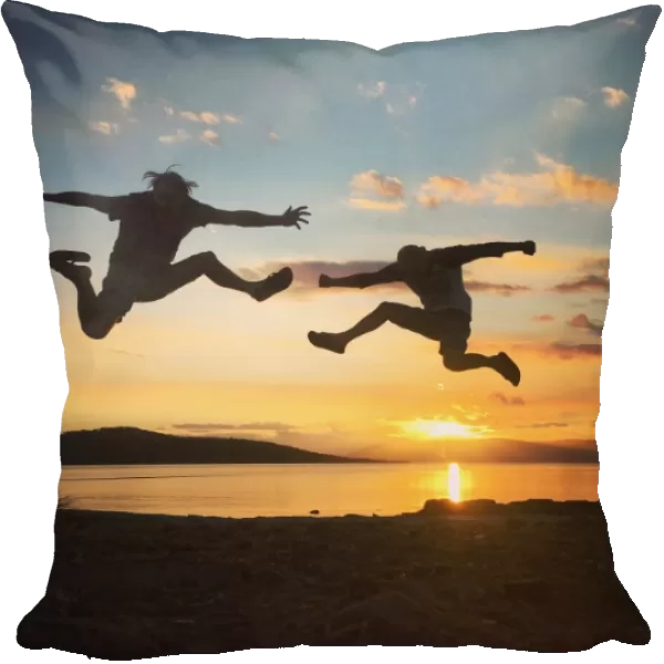 Silhouette of two men jumping into the sunset sky