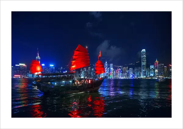 A Traditional Chinese Junk Sailing In Victoria Harbour With View of Hong Kong Island Skyline At Night, Hong Kong, China
