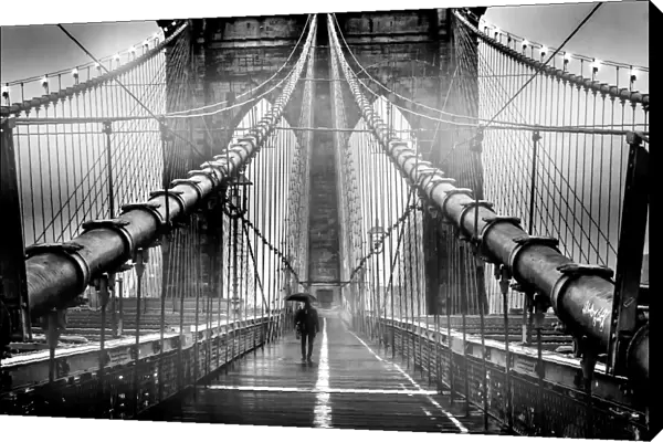 A lone man with umbrella walks along a foggy Brooklyn Bridge at dusk in black and white