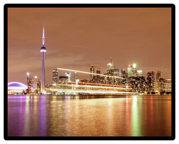 Canada, Ontario, Toronto, Illuminated waterfront skyline and CN Tower reflecting in Lake Ontario with passing ferry light trails