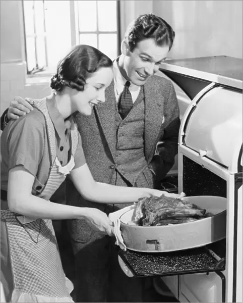 Couple in kitchen, wife taking roast from oven (B&W)