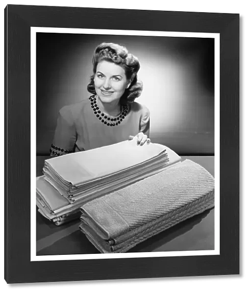 Woman sitting at pile of ironed linen and towels (B&W), portrait