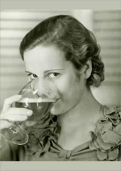 Young woman drinking glass of beer, (B&W), portrait