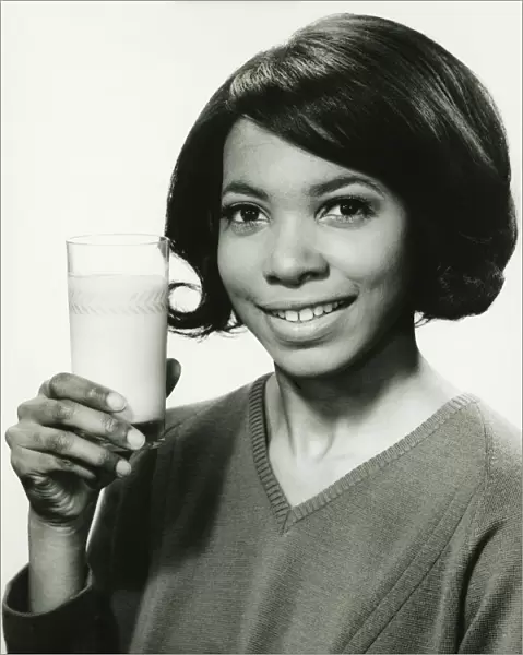 Young woman holding glass of milk in studio, smiling, (B&W), portrait