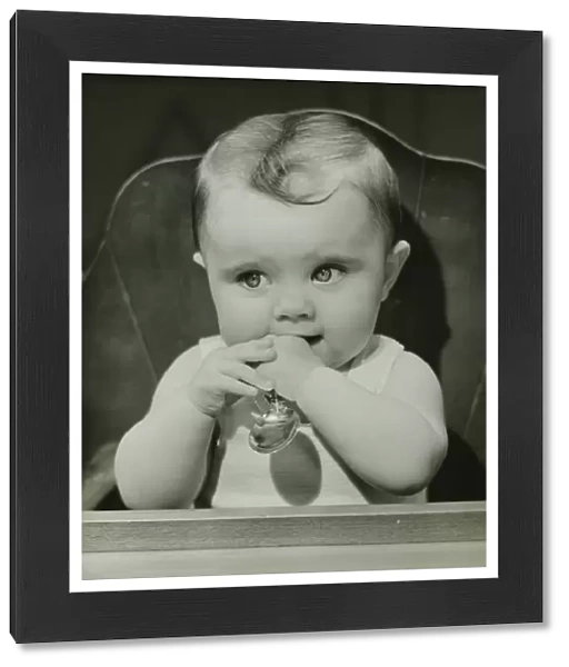 Baby (6-9 months) sitting in high chair, holding spoon, (B&W), portrait