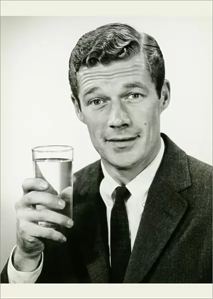 Young businessman holding glass of water, posing in studio, (B&W), portrait